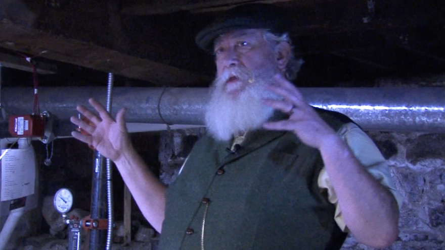 A man in a hat talking in a dark room.
