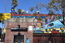 A mural on the wall of El Farolito on Mission Street, facing the northeast corner of the 24th Street BART plaza, by artists Michael J. Rios, Richard Montes, and Tony Machado. Depicts golden figures holding up a silver BART train against the colorful backdrop of the city. 