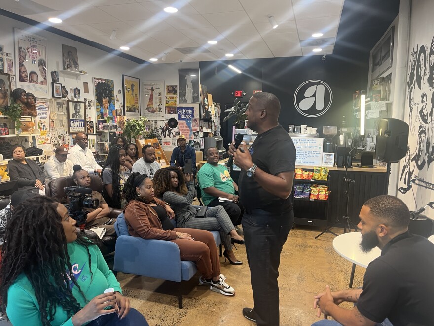 Developer Christopher Dennis holds a microphone as he addresses a group at Archive CLT on Beatties Ford Road. The audience included people interested in real estate and developing properties along the corridor and in similar low-income neighborhoods.