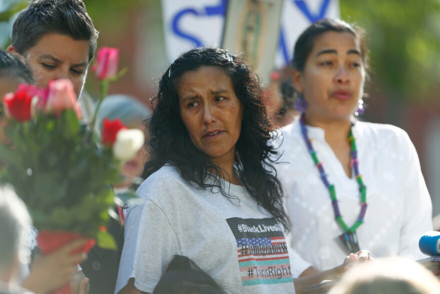 Jeanette Vizguerra wears a gray T-shirt and stands next to other people in a large crowd.