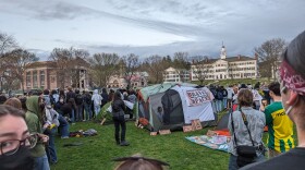 A crowd of people form a ring around a tent on a campus green