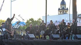 A orchestra performs on a black stage with the Denton historical courthouse in the background