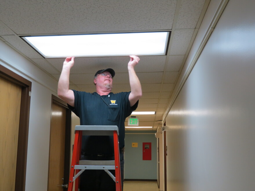 Cleon Ludwick installs the new energy-efficient lights in Western Michigan University's Friedmann Hall. If you look closely, you can see how blue the new lights look compared to the more yellow lights down the hall
