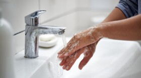 two soapy hands under running water in a sink