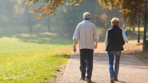 An older couple walks down a dirt pathway.