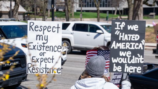 A protester holds two signs up to traffic on South Calhoun Street in downtown Fort Wayne on Saturday. Protesters stretched down both sides of the street, from the intersection of East Berry Street down past the Rousseau Center.