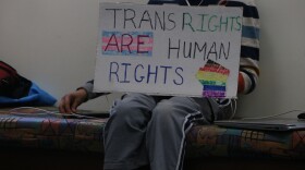 Boy holds sign that reads, "Trans Rights Are Human Rights." Symbol of a fist pumping up to the sky is on the poster.