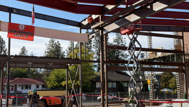 A white steel beam is lifted into place at a building under contruction.