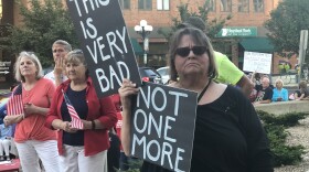 Woman holding two signs with Bloomington mayor and two men in the background