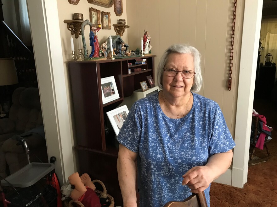 Helen Massie stand in her home in front of a desk with a computer, pictures and figurines.