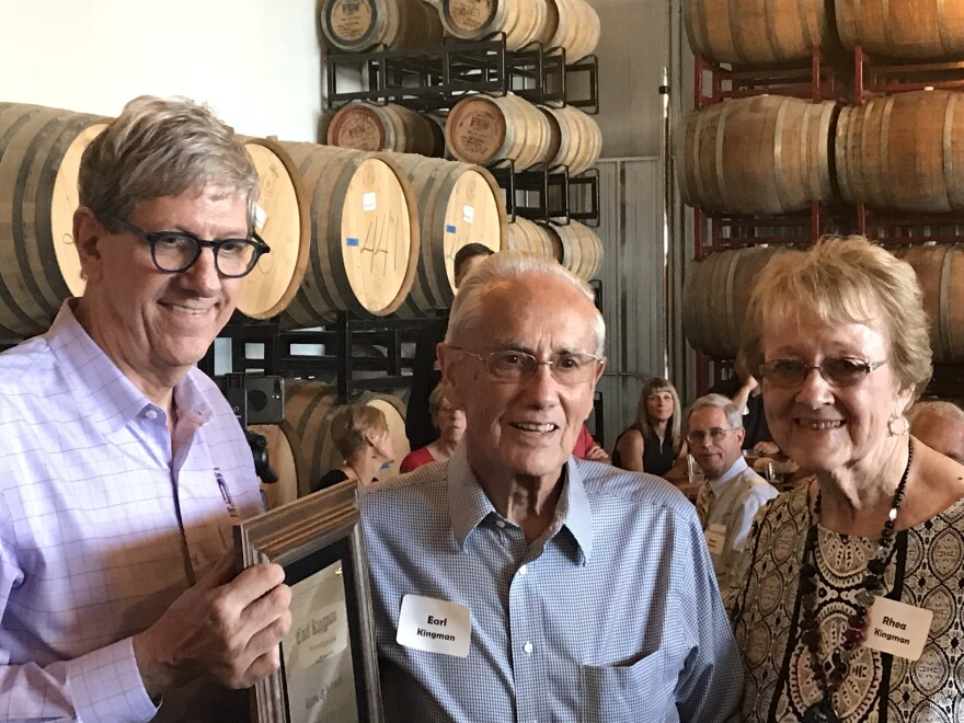 Three people pose for a picture in front of beer barrels