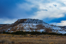 A small, rocky peak with some snow on it in an arid landscape.