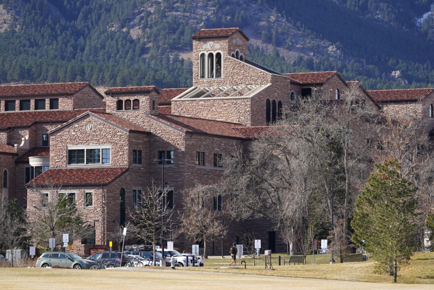 A view of red brick buildings across from a green lawn with trees on the University of Colorado Boulder campus.