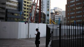 FILE - In this May 8, 2013 file photo, a man looks at his mobile phone near a construction site in Tokyo.  (AP Photo/Greg Baker, File)