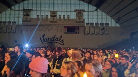 A crowd of hundreds of students hold up lights inside the Kibbie Dome with 'Vandals' written on the wall in black font in the distance.