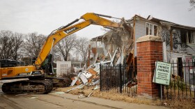 A construction truck begins tearing down a crumbling and graffiti-covered building.