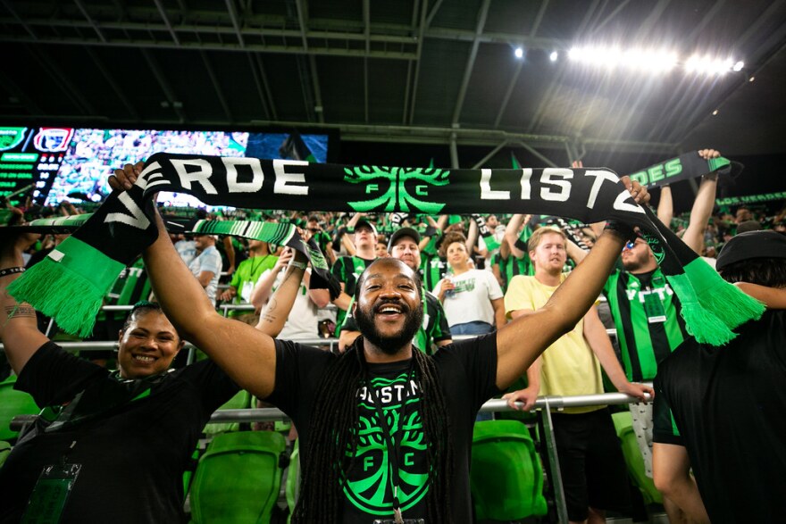 Austin FC fans wearing green jerseys and holding La Verde scarves in the stands at Q2 stadium