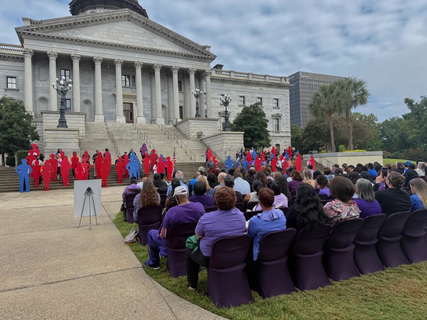 Onlookers and the family members of domestic violence victims stare at 47 silhouettes during Tuesday morning's ceremony. Each silhouette represented someone who died as a result of domestic violence; the lone purple silhouette represents unknown victims.