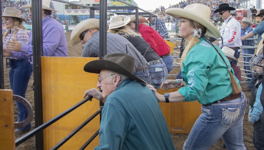 People in cowboy hats next to chutes in an arena.