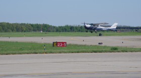 A student pilot in a small blue and white airplane practices touch and go landings and takeoffs at Kalamazoo Battle Creek International Airport in front of a red and white mandatory instruction sign.