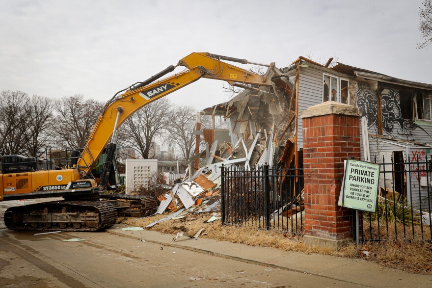 A construction truck begins tearing down a crumbling and graffiti-covered building.