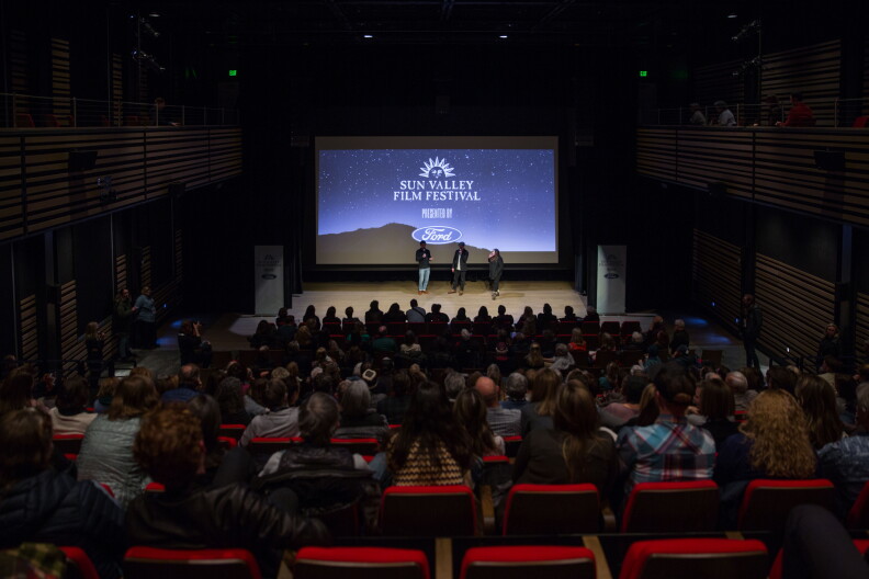 People sit in a dark theater with "Sun Valley Film Festival" projected on a screen on stage.