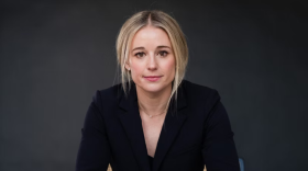 Caroline Gleich sitting with her hands on her knees, smiling slightly at the camera.