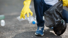 Hands in yellow gloves picking up empty of bottle plastic into bin bag on asphalt, volunteer and purity concept. Enviromental protection.