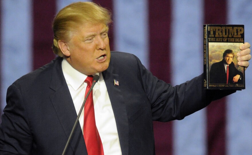 Candidate Trump holds up his book "The Art of the Deal," given to him by a fan in Birmingham, Ala. In the book, he espouses "truthful hyperbole."