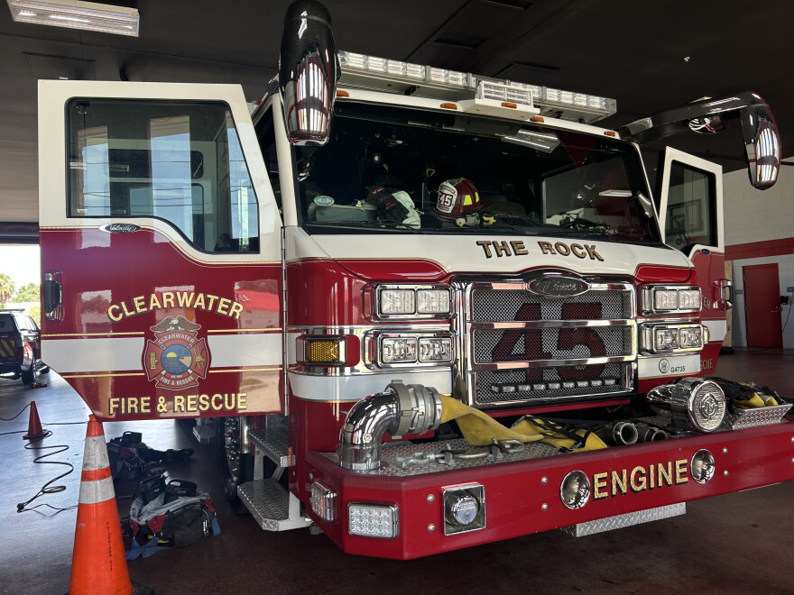 red-and-white Clearwater Fire & Rescue fire truck parked inside a fire station with its front doors open. Firefighting gear lays on the ground around it.