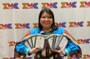 A woman, Jeanette DeDios, poses holding awards in front of a backdrop that has a colorful logo and the words, Indiginous Media Conference.