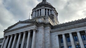 The Washington Legislative Building is pictured, looming over the viewer with a cloudy sky seen behind