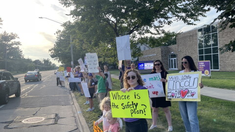 Lakewood parent Gina Rhodes, center with neon sign, protests the district's consolidation plan prior to the Lakewood Board of Education meeting Tuesday.