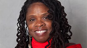 smiling woman in red shirt with black, red and green jacket.