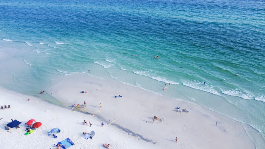 aerial shot of beach chairs, umbrellas and people swimming along white sandy beaches and turquoise water at a Santa Rosa, Florida beach