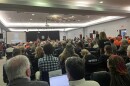 A crowded meeting room with U.S. and Florida flags in the front