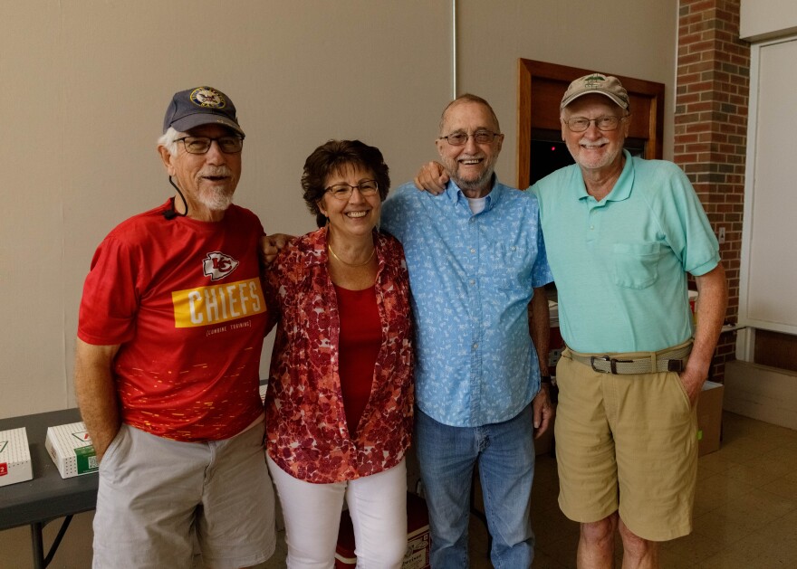 Four friends wrap their arms around each other's backs and smile at the camera