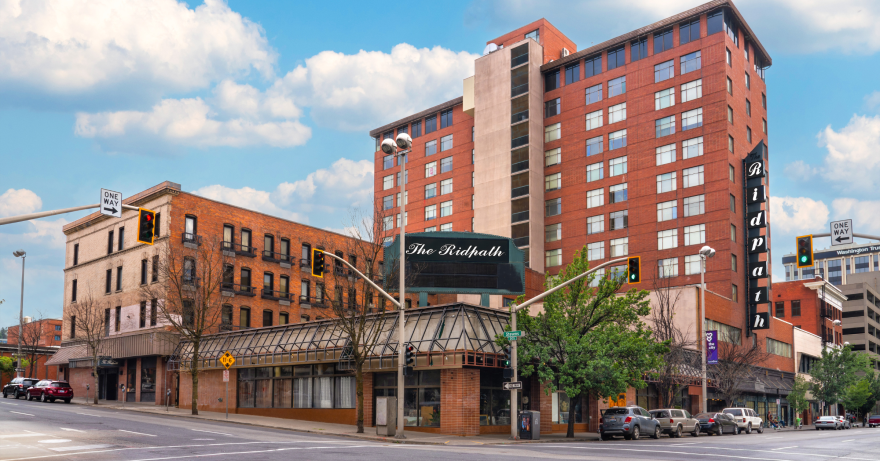 A large brick building against a blue sky has a black sign reading "The Ridpath" in front of it.