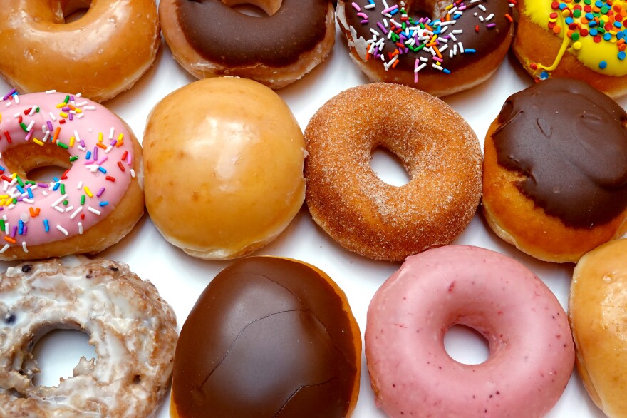 A variety of donuts, some glazed with pink and brown icing, some chocolate-covered without holes, sit in three rows in a box.