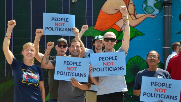 People hold up their fists and hold signs that say, "People not politicians."