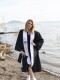 A person poses next to a body of water wearing a graduation gown and holding a cap. 