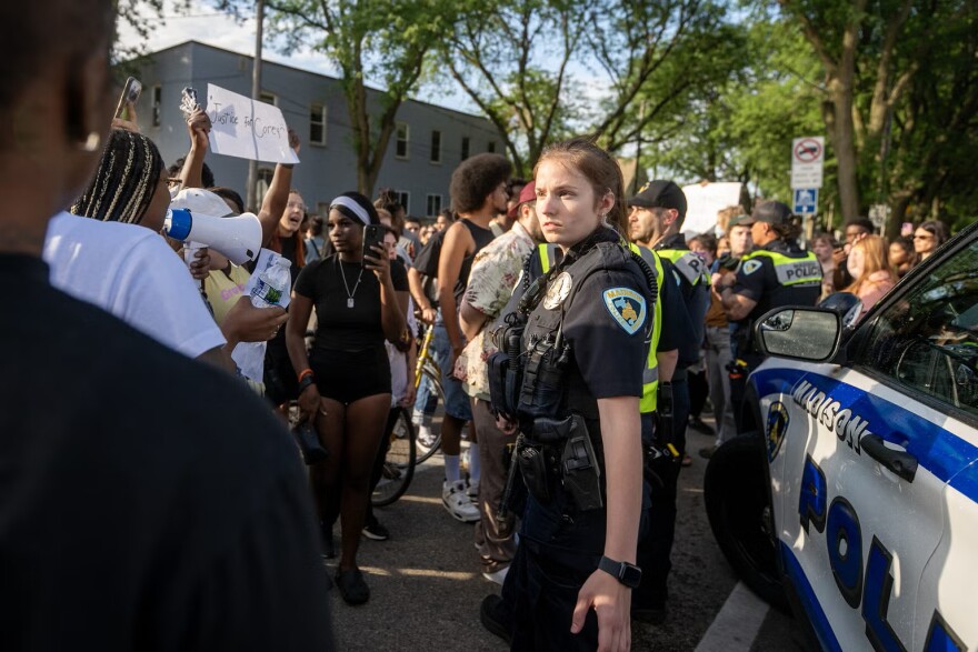 A Madison police officer stands near a squad car as protesters approach Wednesday, July 22, 2026, in Madison, Wis.