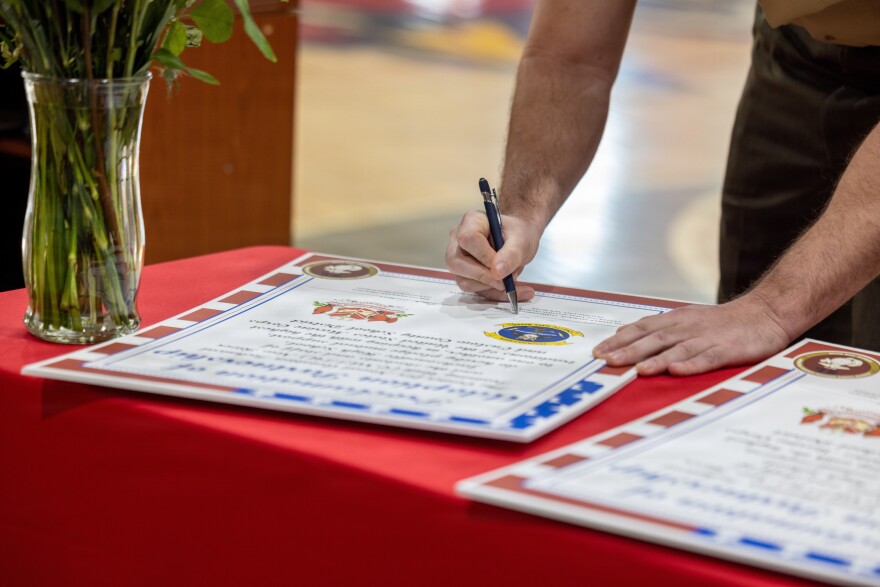U.S. Marine Corps Lt. Col. James P. Psyhogis, commanding officer, Center for Naval Aviation Technical Training Unit New River, signs the adoption proclamation during an Adopt-a-School ceremony at Jacksonville High School in Jacksonville. The final adoption ceremony between Jacksonville High School and the Center for Naval Aviation Technical Training Unit New River marked a significant achievement for Onslow County School District as it reached a 100 percent adoption rate by various units of Marine Corps Installations East and II Marine Expeditionary Force in the Adopt-a-School program.