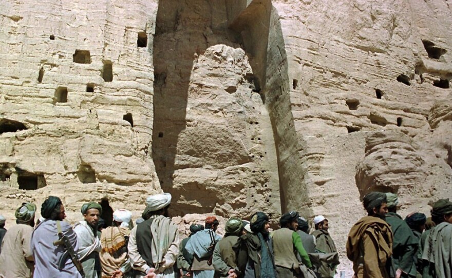 Taliban soldiers stand at the base of a mountain alcove under one of the destroyed Buddha statues in March 2001.