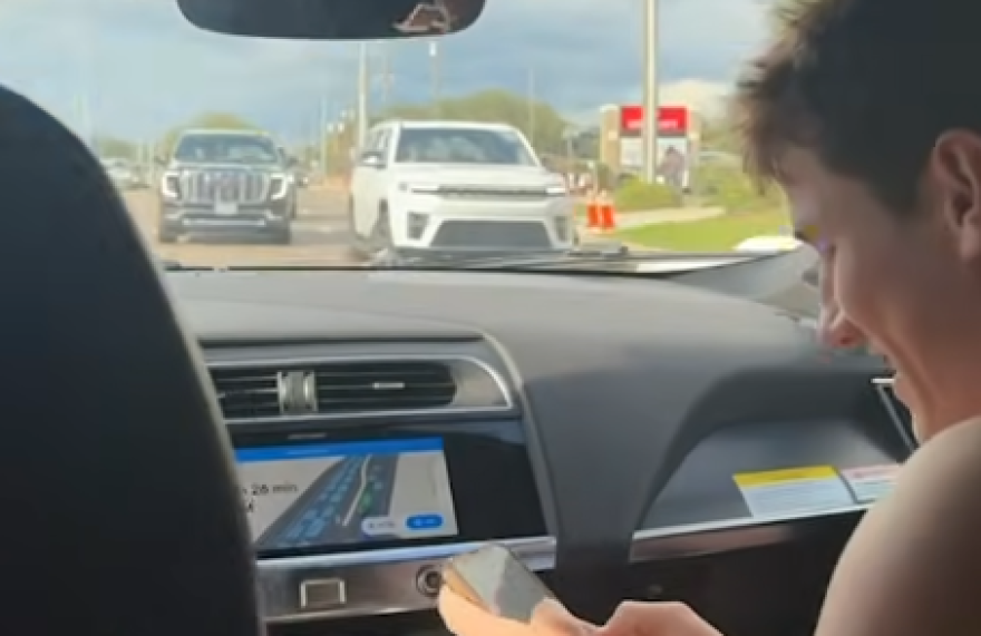 A screengrab shows a man at the right in a car as a white SUV approaches going the wrong way