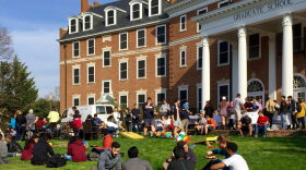 Students sit and stand on a lawn, eating and talking. 