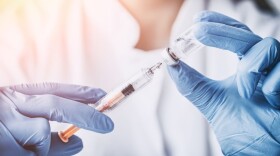 Health care professional's gloved hands holding a vaccine syringe and bottle