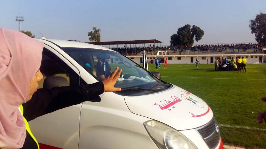 Hanan Abu Qassem motions from the sidelines of a top division professional soccer game in Gaza, poised to treat injured players. Abu Qassem is the first female EMT to staff such games in the Gaza Strip.