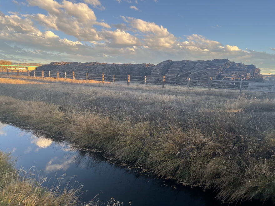 A large pile of railroad ties stacked next to a small creek.