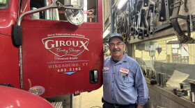 Smiling man in blue workshirt standing by big red red truck which on the door reads 'Giroux Body Shop, Hinesburg, Vermont' 